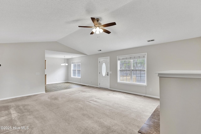 unfurnished living room featuring visible vents, baseboards, lofted ceiling, carpet, and ceiling fan with notable chandelier