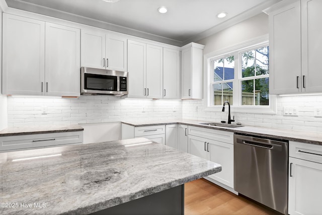 kitchen with stainless steel appliances, a sink, white cabinetry, light wood-style floors, and light stone countertops