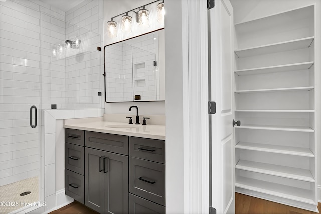 bathroom featuring a stall shower, a walk in closet, vanity, and wood finished floors