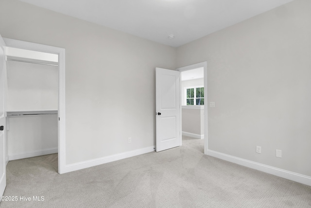 unfurnished bedroom with a spacious closet, baseboards, and light colored carpet