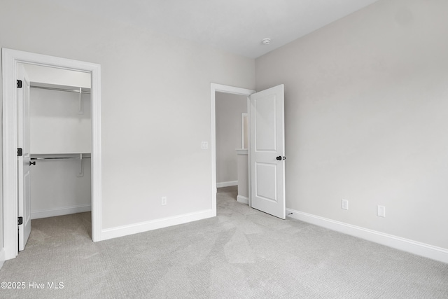 unfurnished bedroom with baseboards, a walk in closet, and light colored carpet