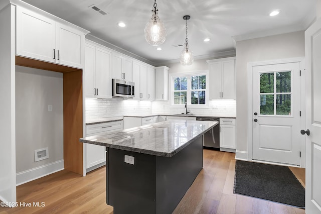 kitchen with pendant lighting, stainless steel appliances, white cabinetry, and a center island