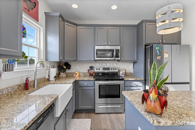 kitchen with light stone counters, hanging light fixtures, gray cabinetry, appliances with stainless steel finishes, and a sink