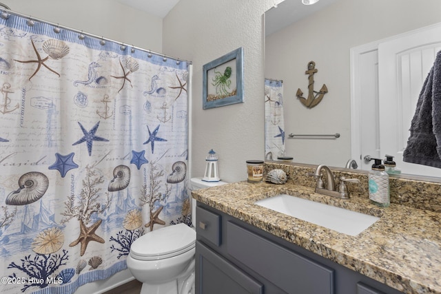 full bathroom featuring a shower with shower curtain, a textured wall, vanity, and toilet