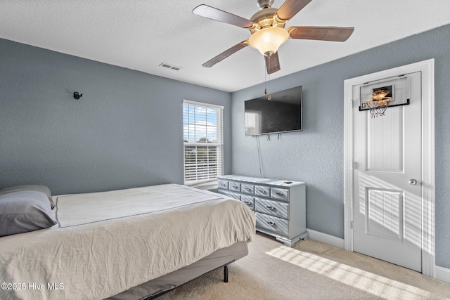 bedroom featuring light colored carpet, visible vents, a textured wall, ceiling fan, and baseboards