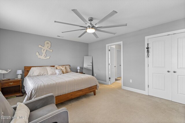 bedroom featuring a closet, light carpet, ceiling fan, ensuite bath, and baseboards