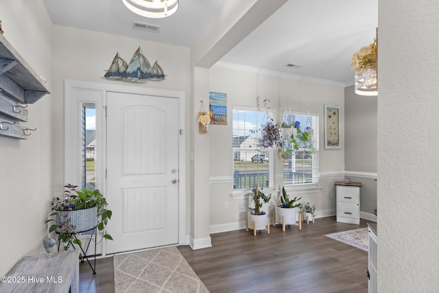 foyer entrance with baseboards, visible vents, dark wood-type flooring, and ornamental molding