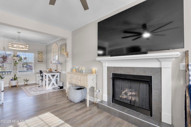 living room with a ceiling fan, a fireplace, ornamental molding, and wood finished floors