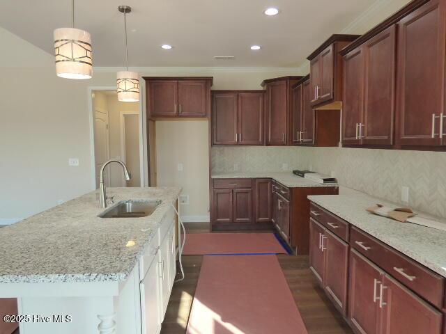 kitchen with light stone counters, dark wood-type flooring, a center island, hanging light fixtures, and a sink