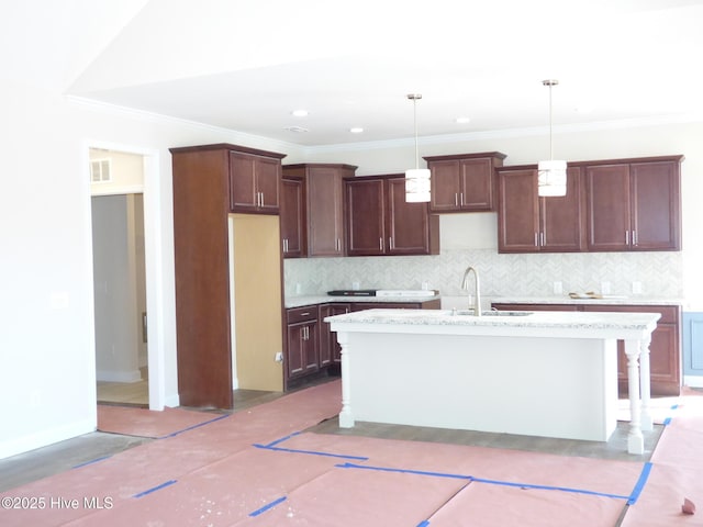 kitchen with a sink, visible vents, backsplash, an island with sink, and pendant lighting