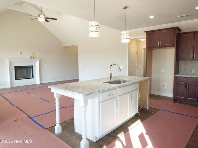 kitchen with a sink, white cabinetry, open floor plan, light stone countertops, and decorative light fixtures