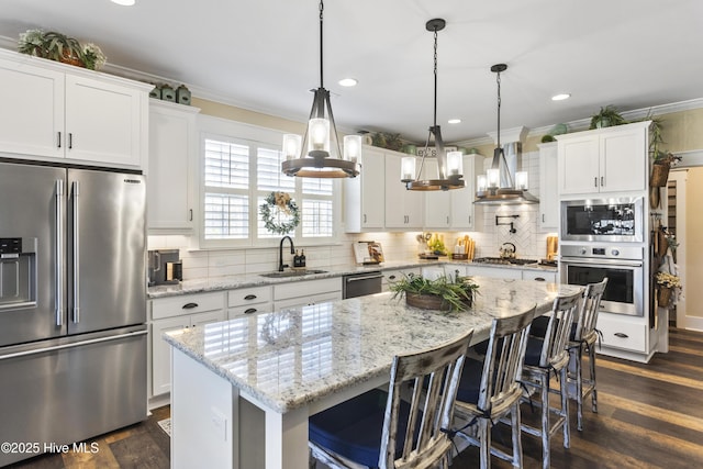 kitchen with appliances with stainless steel finishes, ornamental molding, dark wood-style flooring, wall chimney range hood, and a sink