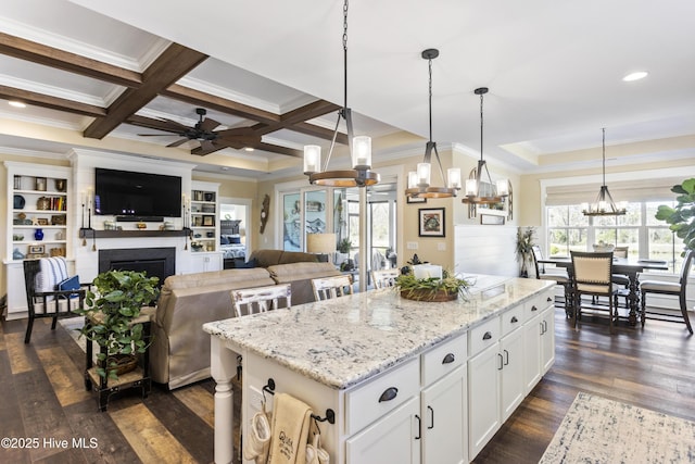 kitchen with a center island, a fireplace, crown molding, dark wood-type flooring, and coffered ceiling