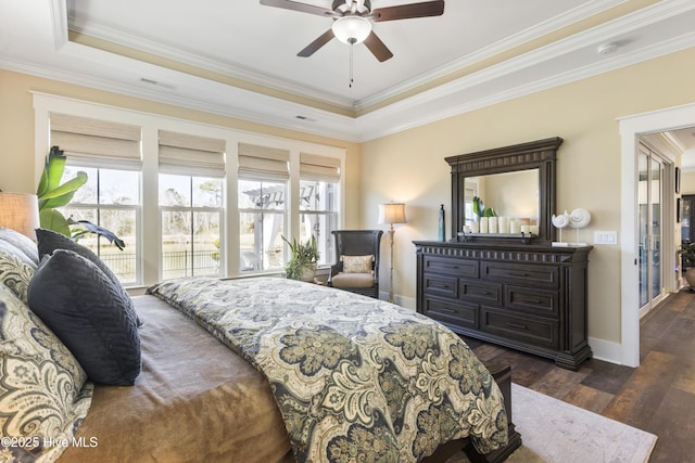 bedroom featuring ornamental molding, a tray ceiling, dark wood-type flooring, and baseboards