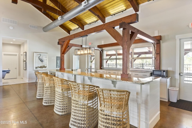 bar with visible vents, beam ceiling, stainless steel microwave, and finished concrete flooring