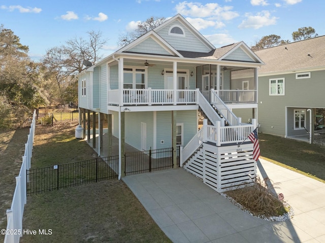 coastal home featuring a porch, concrete driveway, ceiling fan, a front lawn, and stairs