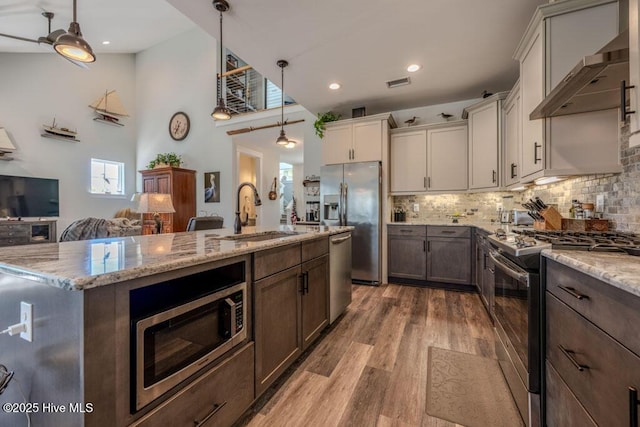 kitchen with white cabinets, stainless steel appliances, wall chimney range hood, pendant lighting, and a sink