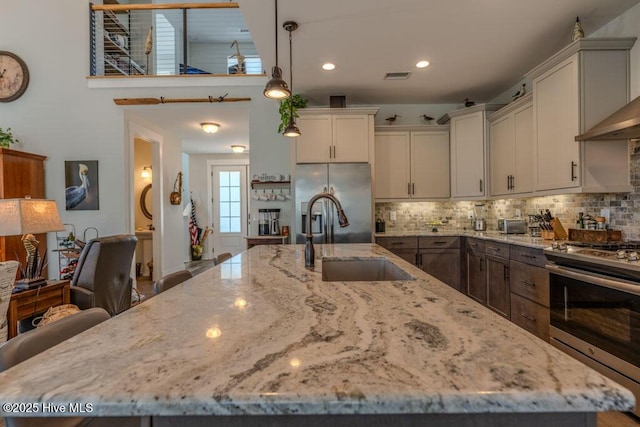 kitchen featuring decorative light fixtures, light stone countertops, a kitchen island with sink, stainless steel appliances, and a sink