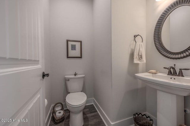 half bath featuring a sink, wood finished floors, toilet, and baseboards