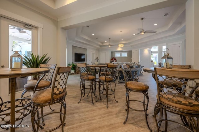 dining room with visible vents, a ceiling fan, ornamental molding, light wood-type flooring, and a tray ceiling