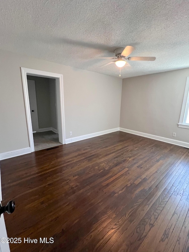 empty room with a textured ceiling, dark wood-type flooring, a ceiling fan, and baseboards