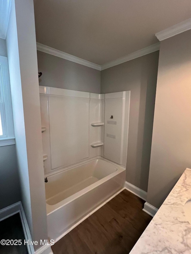 full bath featuring baseboards, tub / shower combination, wood finished floors, and crown molding