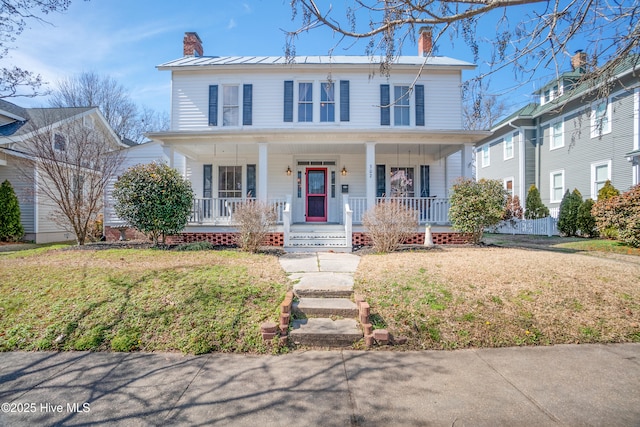 view of front of home with a chimney, covered porch, a front yard, a standing seam roof, and metal roof