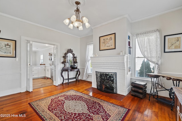 interior space with crown molding, wood-type flooring, an inviting chandelier, a brick fireplace, and baseboards