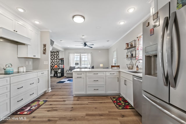 kitchen featuring stainless steel appliances, light countertops, white cabinetry, a sink, and a peninsula