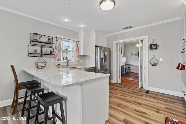 kitchen featuring a peninsula, a sink, visible vents, a kitchen breakfast bar, and appliances with stainless steel finishes