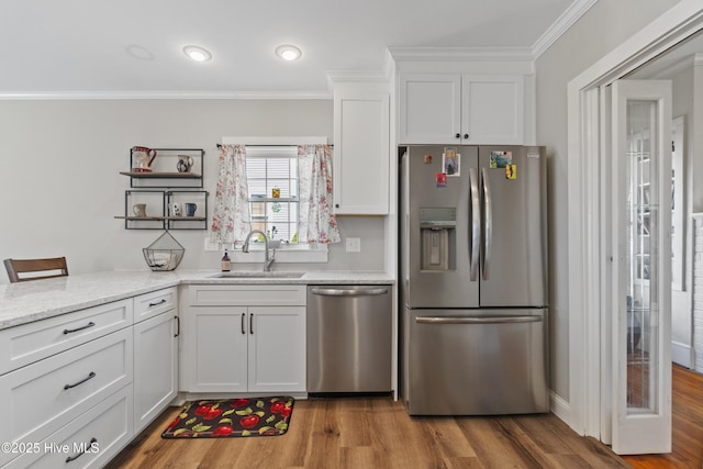 kitchen with stainless steel appliances, white cabinets, a sink, and ornamental molding