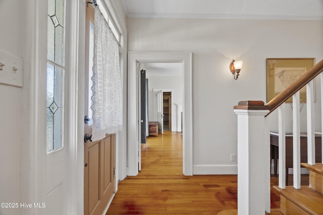 hallway with crown molding, stairway, a healthy amount of sunlight, light wood-type flooring, and baseboards