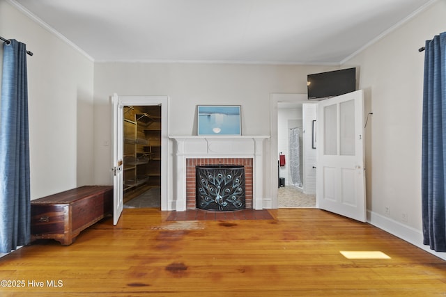 unfurnished living room featuring ornamental molding, a brick fireplace, baseboards, and wood finished floors