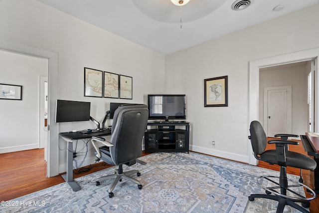 office featuring a ceiling fan, visible vents, baseboards, and wood finished floors