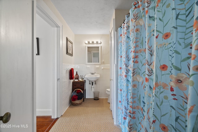 full bathroom with a shower with shower curtain, toilet, wainscoting, a textured ceiling, and tile walls