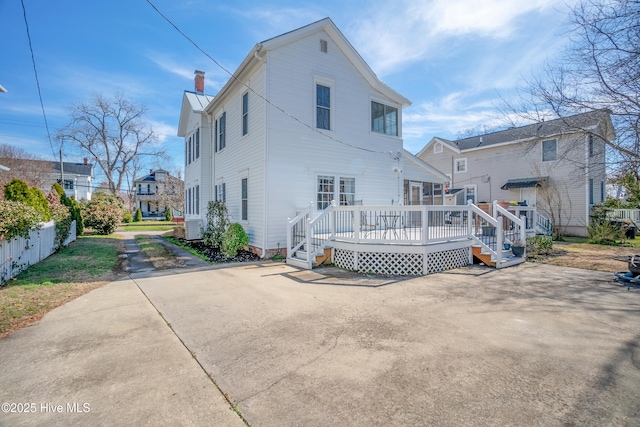 rear view of house featuring fence, a chimney, and a wooden deck