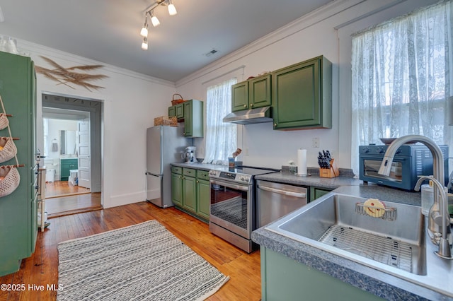 kitchen with light wood-type flooring, under cabinet range hood, green cabinets, and stainless steel appliances