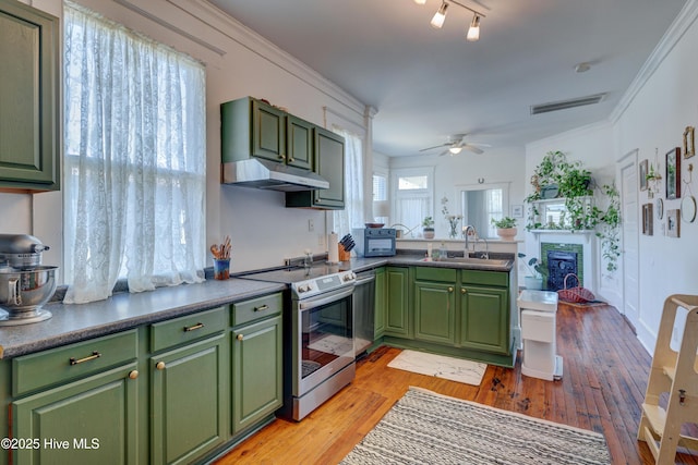 kitchen with stainless steel appliances, dark countertops, a sink, green cabinetry, and under cabinet range hood