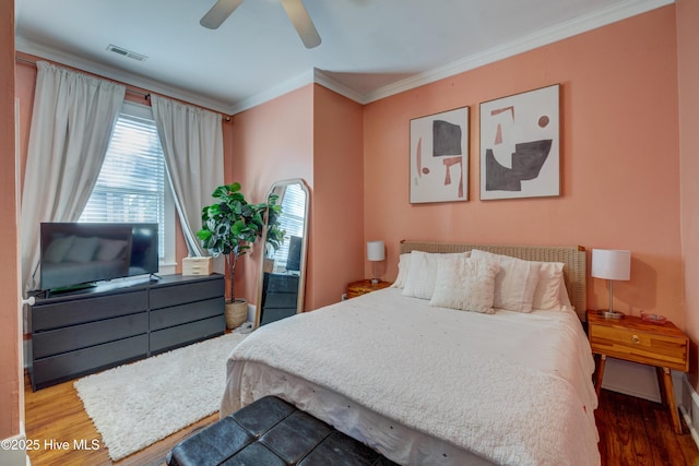 bedroom featuring a ceiling fan, crown molding, visible vents, and wood finished floors