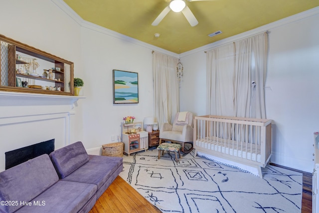 bedroom featuring crown molding, visible vents, a ceiling fan, wood finished floors, and baseboards