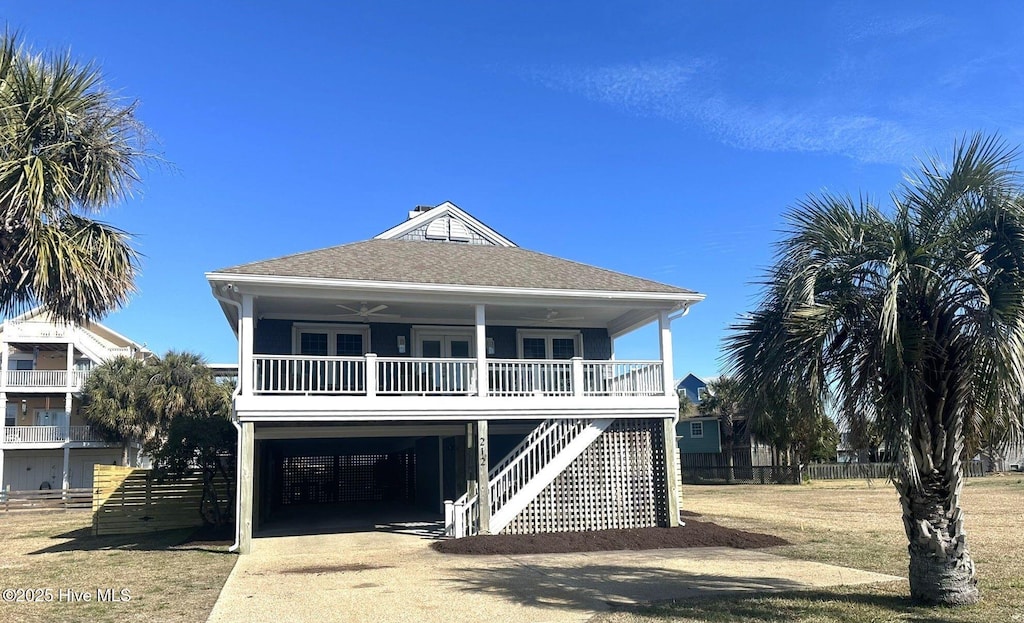 raised beach house featuring concrete driveway, roof with shingles, stairs, a porch, and a carport