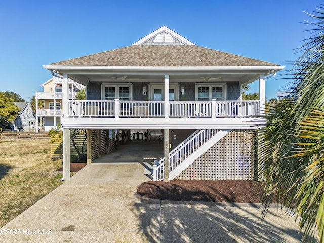 beach home featuring a porch, a shingled roof, stairway, a carport, and driveway