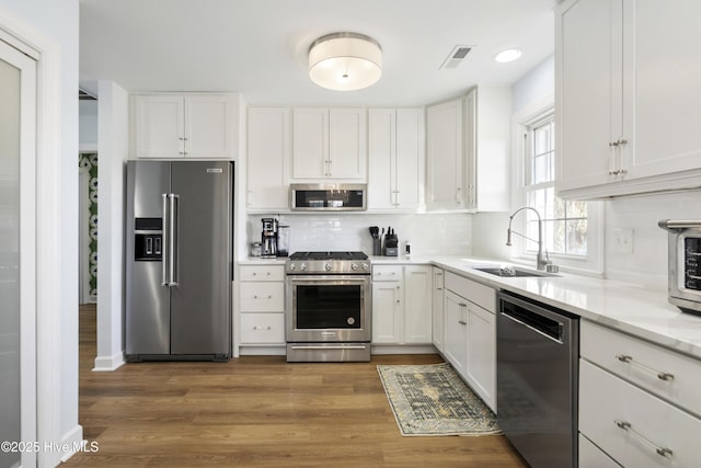 212 Florida Ave, Carolina Beach, NC 28428 - kitchen with appliances with stainless steel finishes, a sink, backsplash, white cabinetry, and dark wood-style floors