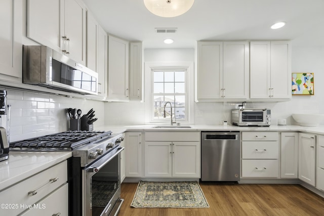 212 Florida Ave, Carolina Beach, NC 28428 - kitchen featuring appliances with stainless steel finishes, a sink, white cabinetry, backsplash, and wood finished floors