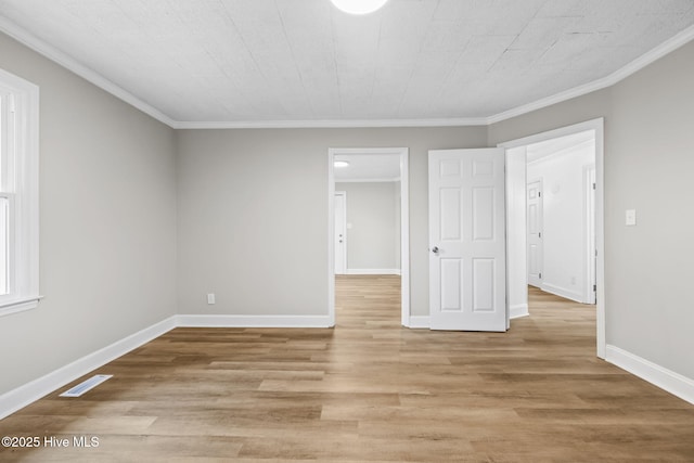 interior space with light wood-style floors, visible vents, crown molding, and baseboards