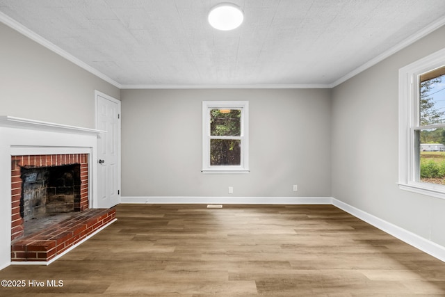 unfurnished living room with a brick fireplace, crown molding, baseboards, and wood finished floors