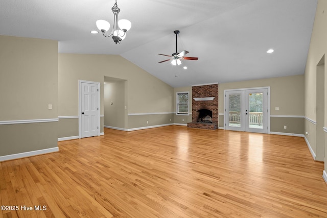 unfurnished living room featuring ceiling fan with notable chandelier, baseboards, vaulted ceiling, light wood-style floors, and a brick fireplace