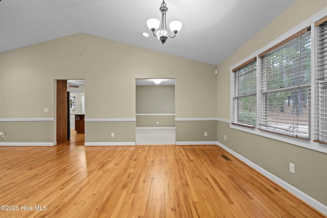 spare room with wood finished floors, visible vents, baseboards, vaulted ceiling, and an inviting chandelier