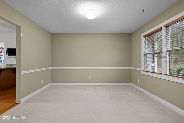 unfurnished room featuring light carpet, a textured ceiling, and baseboards