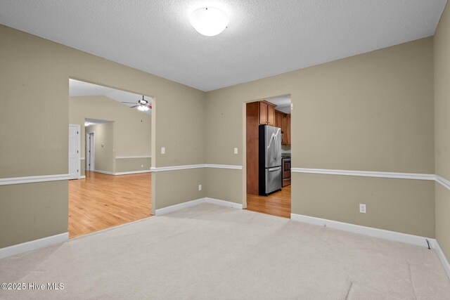 empty room with light colored carpet, a ceiling fan, vaulted ceiling, a textured ceiling, and baseboards